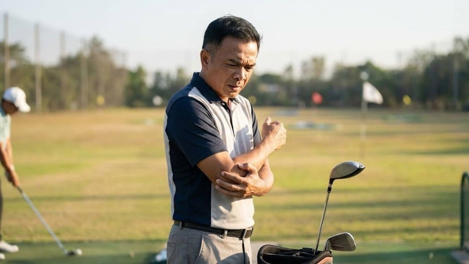 นักกอล์ฟยืนกุมข้อศอกที่มีอาการบาดเจ็บ (Golfer's Elbow) จากแรงสะเทือนของการตีเหล็ก สาเหตุสำคัญที่ควรเปลี่ยนมาใช้ก้าน Fujikura MCI 2025 เพื่อถนอมร่างกาย